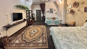A cozy bedroom with a large bed, a TV on a shelf, a chandelier, and a patterned rug.