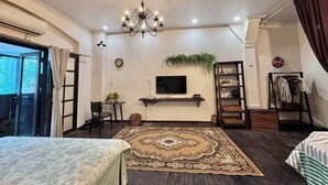 A modern bedroom with a large bed, a TV mounted on the wall, a chandelier, and a view of the outdoors.