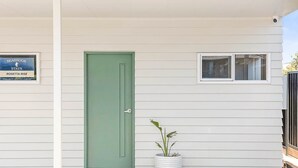 A green door, a potted plant, and a signboard on a white building facade. - Rosetta Rise, Bright Roomy Home with Ocean Views (Hayborough)