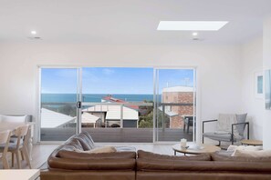 A modern living room with a large sliding glass door leading to a balcony with a view of the sea. - Rosetta Rise, Bright Roomy Home with Ocean Views (Hayborough)
