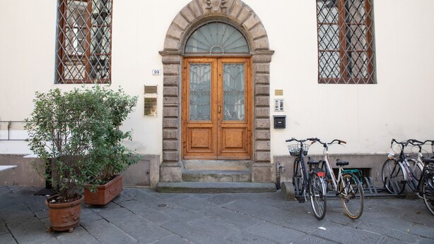 A building with a wooden double door, two windows with metal grilles, and a potted plant in front. - Dimora San Paolino in Center Town (Lucca)