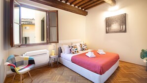 A bedroom with a large bed, a chair, a nightstand, a window, and a painting on the wall. - Dimora San Paolino in Center Town (Lucca)