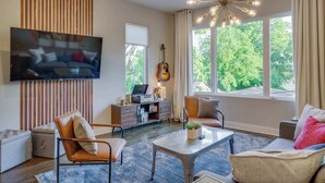 A living room with a flat-screen TV, a guitar, a coffee table, and a sofa. - Weekend getaway: 2 rooftop homes, sleeps 24, near Broadway, Nashville (Nashville)