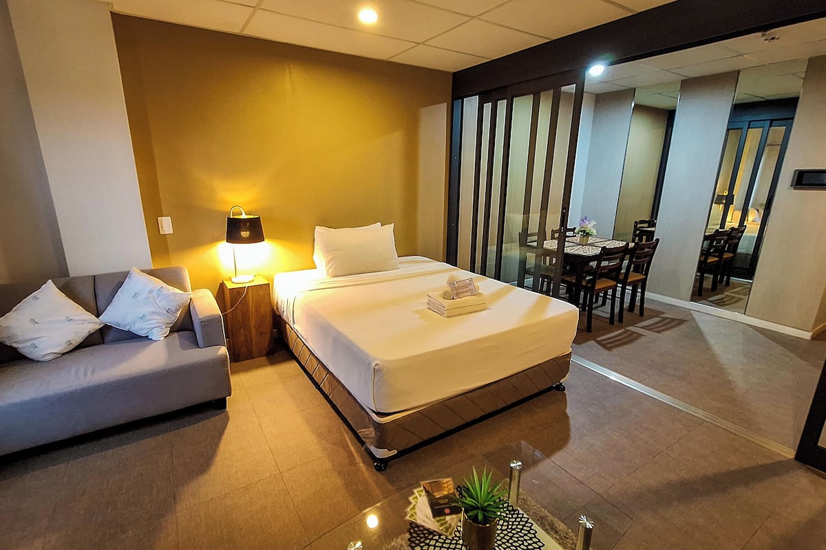 Une chambre d’hôtel avec un lit, un canapé, une table avec une plante et, au fond, un coin repas.