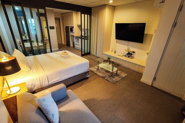 Una habitación de hotel moderna con una cama grande, un sofá, un televisor y una kitchenette.