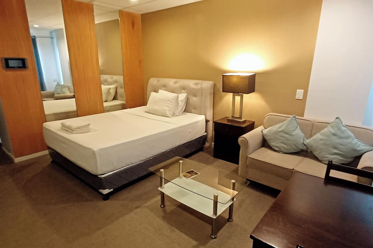 Une chambre d’hôtel avec un lit, une table basse en verre, un canapé, une lampe et un miroir.