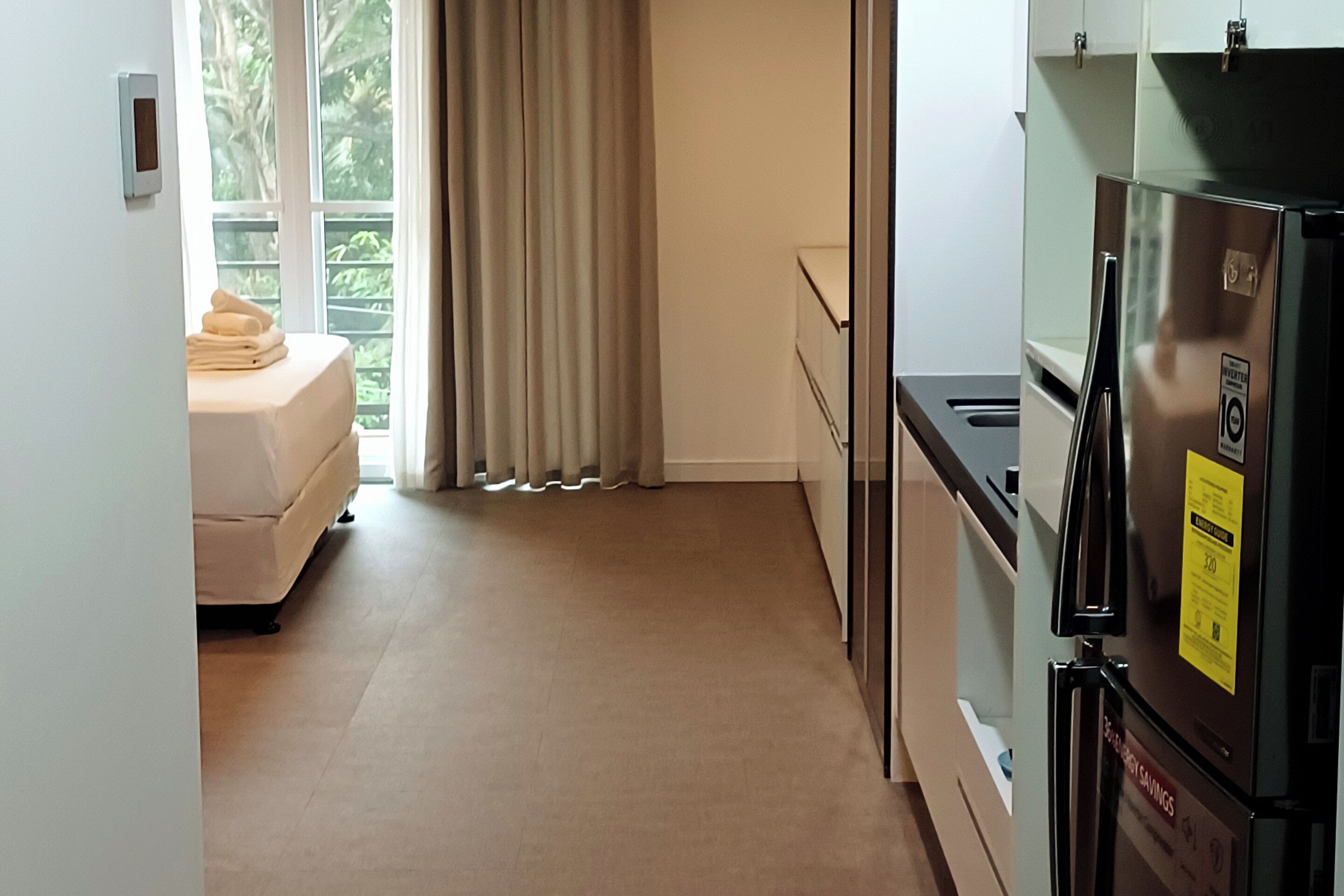 Cocina compacta con refrigerador, una superficie de apoyo pequeña y un ventanal con cortinas.