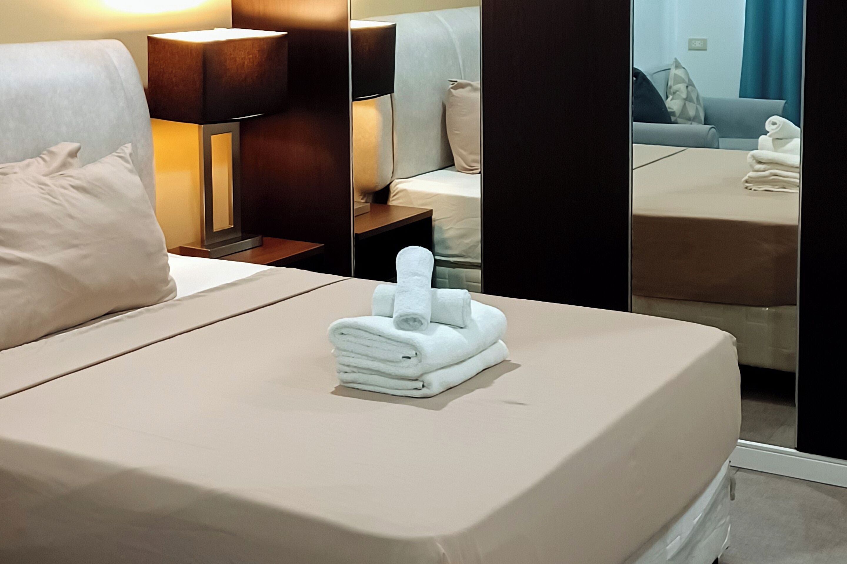A neatly made bed with a folded towel and a small stack of towels on the side.