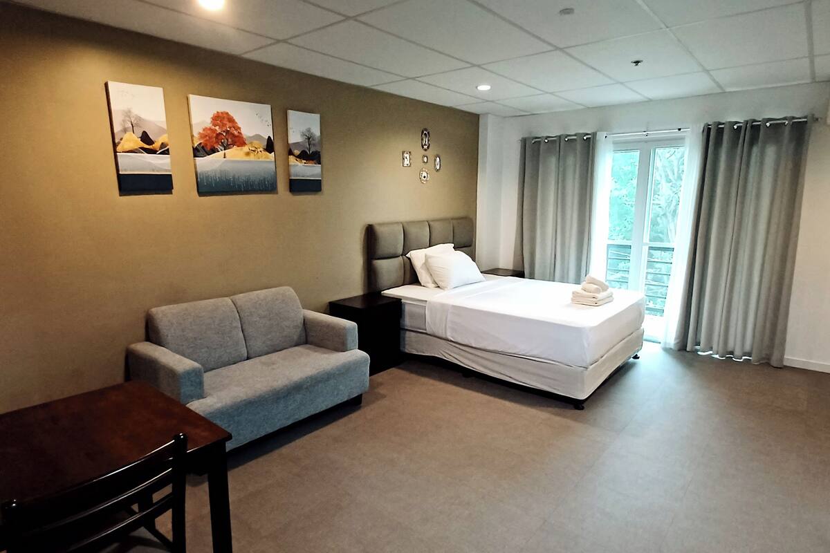 Une chambre d’hôtel avec un lit, un canapé gris, une table en bois et des œuvres d’art accrochées au mur.
