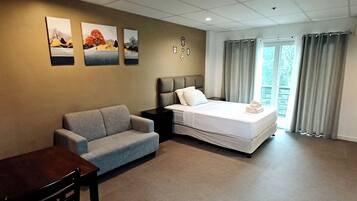 Et hotelværelse med en seng, en grå sofa, et træbord og billedkunst på væggen.
