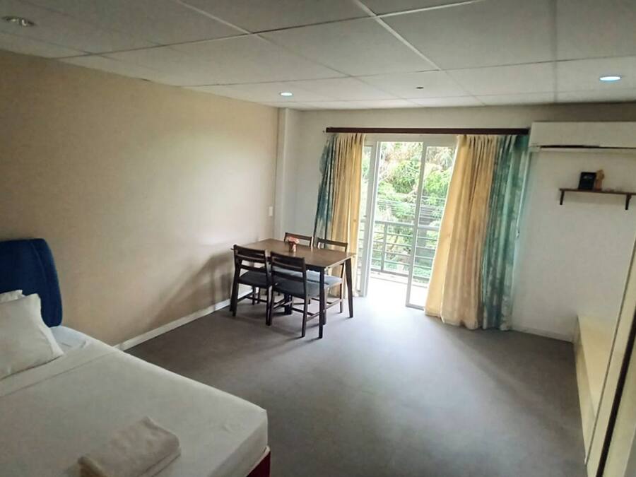 A hotel room with a bed, a dining table with chairs, a small table with a vase, and a window with curtains.