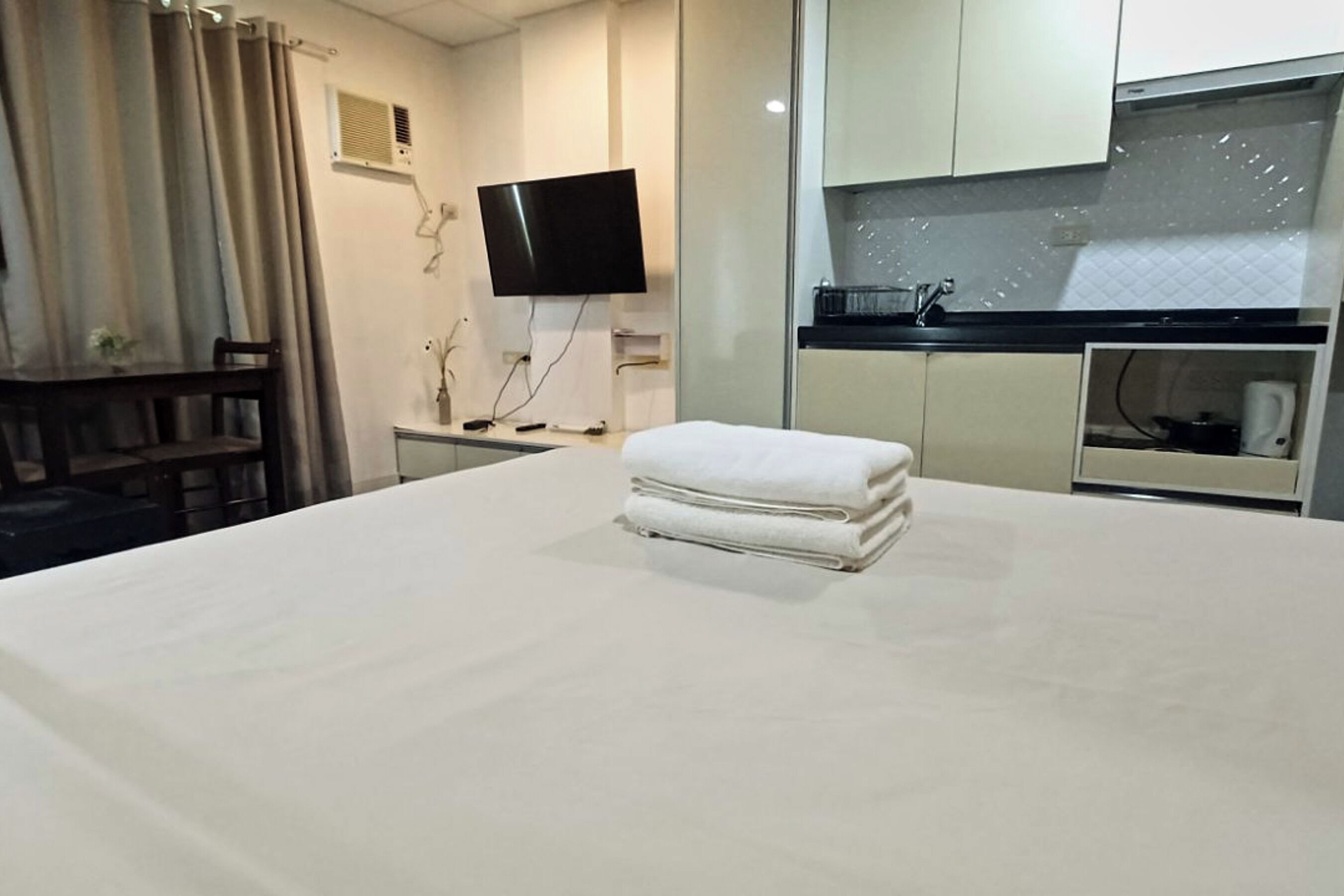 A hotel room with a bed, a TV, a small kitchenette, and a window with curtains.