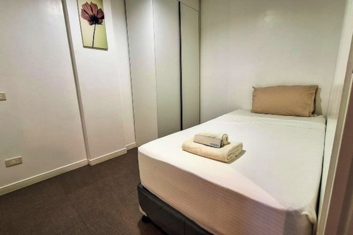 A neatly made bed with a pillow and a folded towel, a wall-mounted mirror, and a framed picture of a flower.