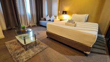 Een hotelkamer met een bed, een glazen bijzettafeltje, een bank, een lamp en een plant.