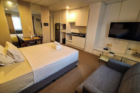 A hotel room with a bed, a desk, a chair, a sofa, a TV, a kitchen area, and a mirror. - Smart Condominium powered by Cocotel (Cagayan de Oro)