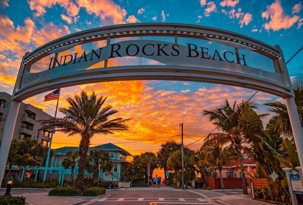 A sign reading 'Indian Rocks Beach' with palm trees and a sunset in the background.