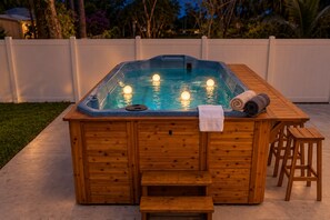 A wooden hot tub with a built-in bench and stools, surrounded by a white fence.