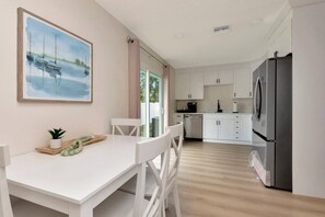 A modern kitchen with white cabinets, a stainless steel refrigerator, and a dining area with a white table and chairs.