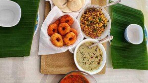 Un tavolo con diversi piatti indiani, tra cui pane, snack fritti e curry, serviti su foglie di banano.