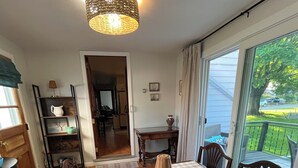 Ein Essbereich mit einem Holztisch, karierten Platzsets und Stühlen. Auf dem Tisch steht eine Lampenschirm aus Weidengeflecht, und durch eine Glastür ist ein Blick ins Freie möglich.