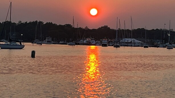 Ein Yachthafen mit angestaubten Booten und einem Sonnenuntergang im Hintergrund.