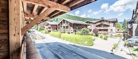 Un edificio de madera con un balcón que da a un pueblo con casas tradicionales y montañas al fondo.