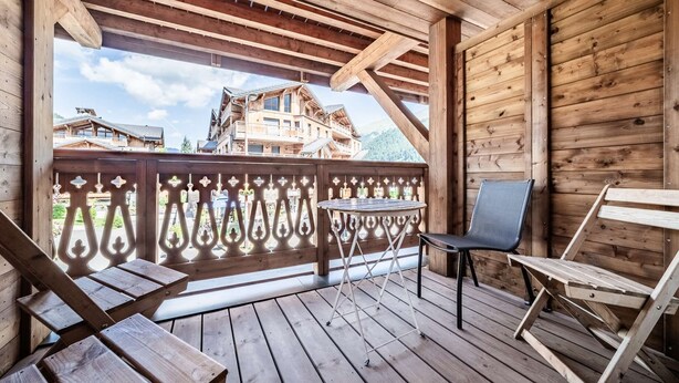 A wooden deck with two chairs and a table, overlooking a mountain lodge.