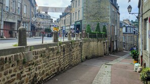 A stone wall with a paved walkway, historic buildings, and a sign for 'Quartier des Merveilleuses.'