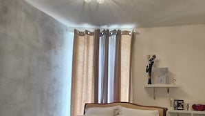 A bedroom with a bed, curtains, a shelf with items, and a ceiling light fixture.