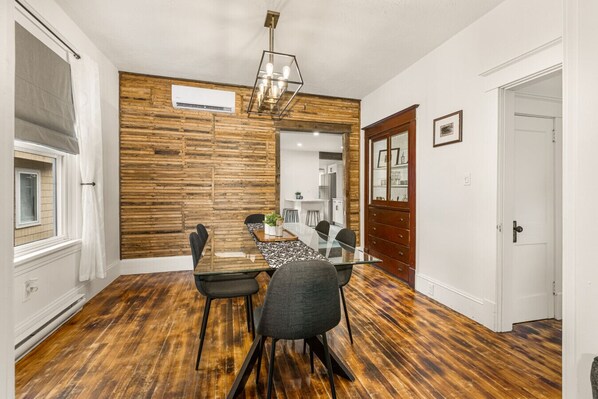 A dining area with a wooden wall, a glass table, and black chairs.