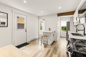 A modern kitchen with white cabinetry, a built-in stove, and a window overlooking the garden. - The Big City Stay | Sleeps 11 | Walkable Location (Moncton)