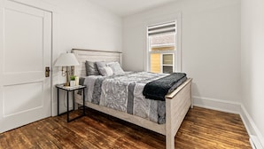 Un dormitorio con cama de madera, una mesita de noche con lámpara y una ventana con persianas.