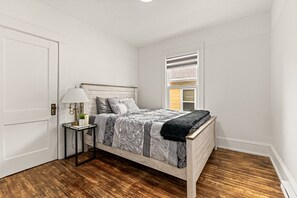 Ein Schlafzimmer mit einem hölzernen Bett, einem Nachttisch mit Lampe und einem Fenster mit Jalousien.