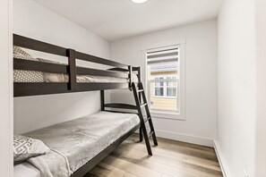 Habitación con literas, una escalera, una ventana con persianas y vista a un edificio.