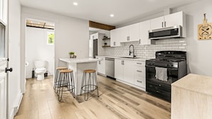 Una cocina moderna con armarios blancos, una estufa negra y taburetes de madera.
