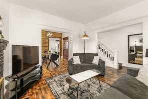 Una sala de estar moderna con un televisor de pantalla plana, un sofá gris, una mesa de centro y una escalera que lleva a otro nivel.