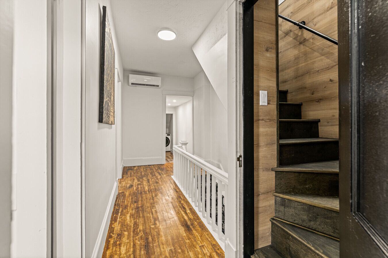 A hallway with wooden flooring, white walls, and a black staircase.