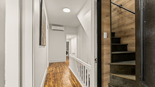 Un couloir doté d’un plancher en bois, de murs blancs et d’un escalier noir.