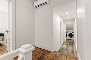 A clean, modern hallway with a wooden floor, white walls, and a laundry area visible in the distance.
