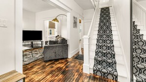 Un escalier recouvert d’une moquette à motifs, un canapé gris, un téléviseur et un plancher en bois.