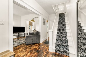 A staircase with patterned carpet, a gray sofa, a television, and a wooden floor.