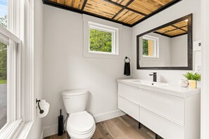 Une salle de bain moderne avec des toilettes blanches, un lavabo et un miroir. Il y a une fenêtre au-dessus des toilettes et une petite fenêtre au-dessus du lavabo.
