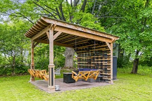 A wooden pergola with a swing set and seating area, surrounded by lush greenery.