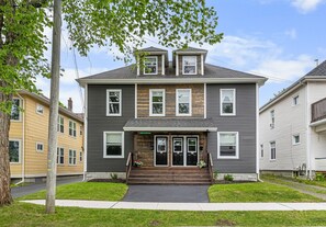 A two-story residential building with a front porch, a small garden, and a visible garage.