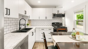 Una cocina moderna con armarios blancos, una estufa negra y un ventanal con vista a vegetación.