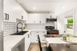 A modern kitchen with white cabinets, a black stove, and a window with a view of greenery.