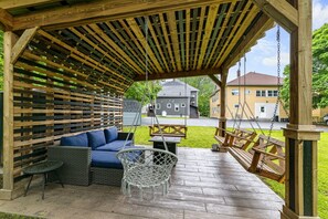 Un espace extérieur aménagé avec une zone salon couverte, comprenant une balançoire, un canapé bleu et un fauteuil en osier.