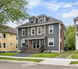 A two-story residential building with a front porch, a staircase, and a driveway. - Clean & Modern 1BR | 4 Guests | Parking & Wi-Fi (Moncton)