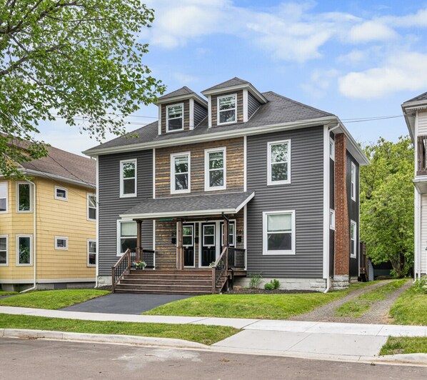 A two-story residential building with a front porch, a staircase, and a driveway.
