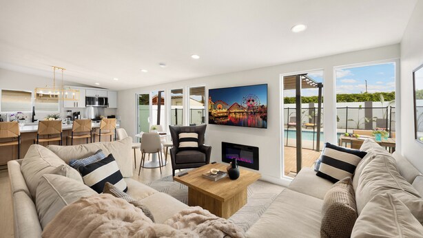 Ein modernes Wohnzimmer mit einer Couch, einem Couchtisch und einem Kamin. Es gibt einen Essbereich mit Stühlen und einem Tisch, und im Hintergrund eine Küche.